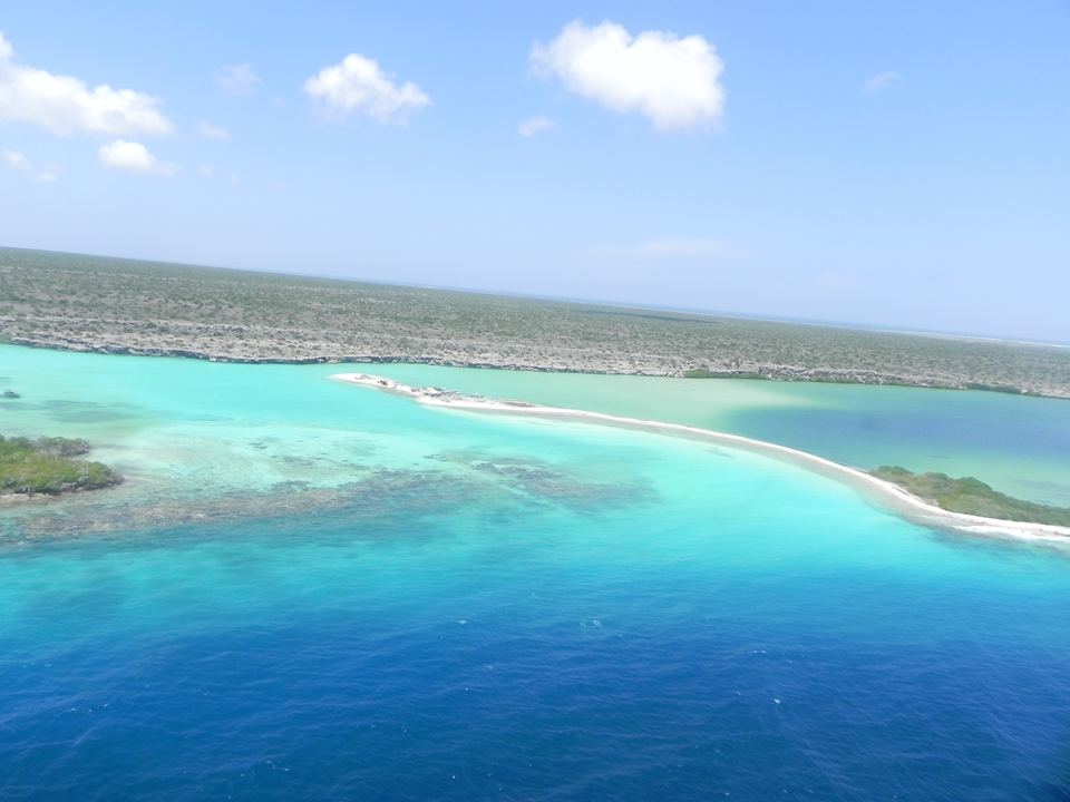 Aerial view of turquoise reef flats and a white sand spit at La Tortuga