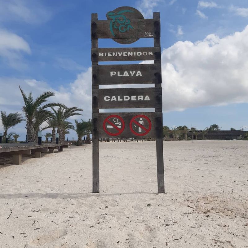 Welcome sign at Playa Caldera with palms and a wooden boardwalk